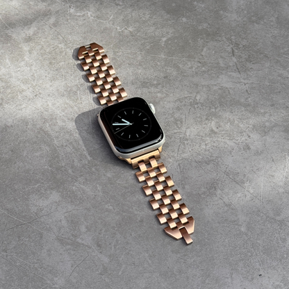 Rose gold multi link Apple Watch band lying flat on grey concrete. Modern brushed matte stainless steel iWatch strap, compatible with Apple Watch 38mm to 49mm, Series 1-11, SE and Ultra