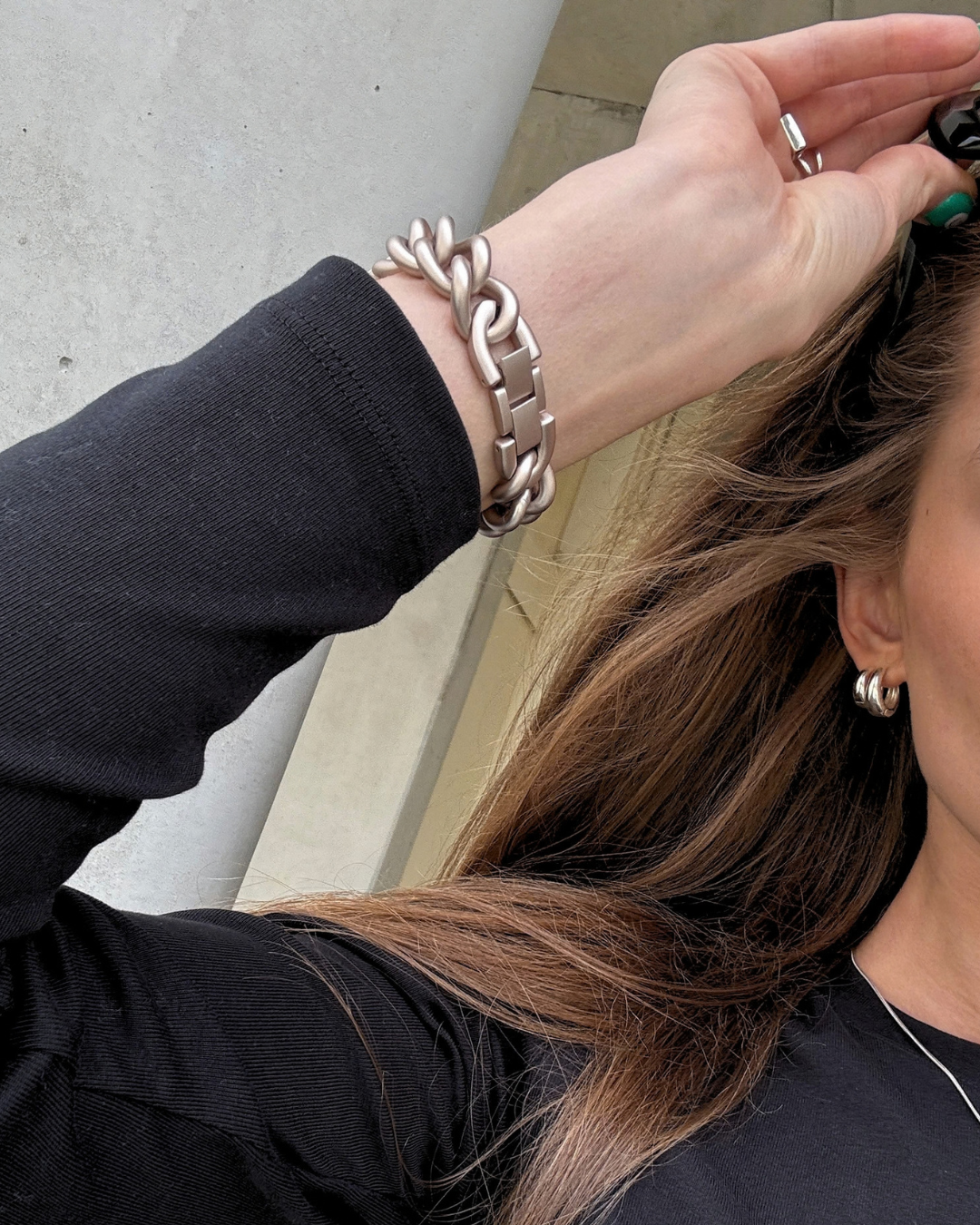 A close-up lifestyle shot of a woman wearing a chunky starlight chain link Apple Watch Band on her wrist, with her hand adjusting her hair.