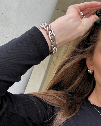 A close-up lifestyle shot of a woman wearing a chunky starlight chain link Apple Watch Band on her wrist, with her hand adjusting her hair.